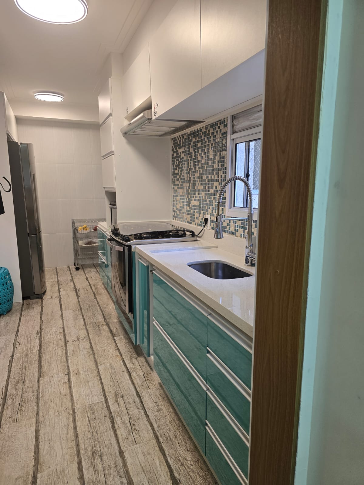 Cozinha planejada com armários verdes e bancada em quartzo do apartamento no Condomínio Alegria, Guarulhos